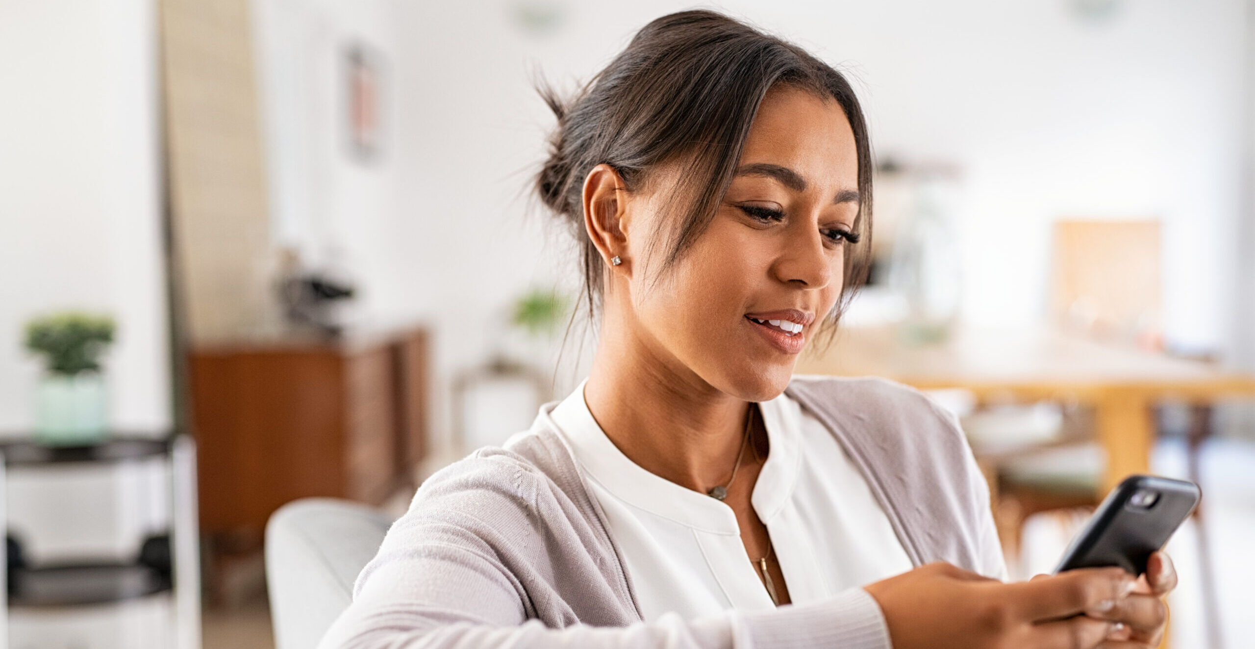 Mature african woman sitting on couch at home using smartphone. Black woman relaxing on the sofa while messaging with a cellphone at home. Happy mature indian woman typing on mobile phone in living room.